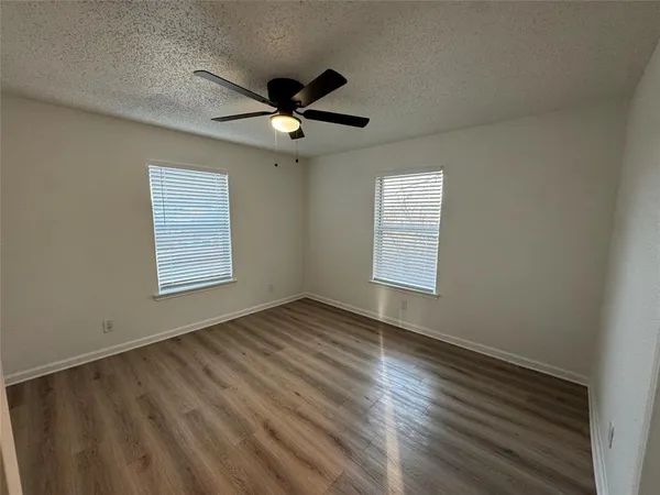 an empty room with wooden floor ceiling fan and windows