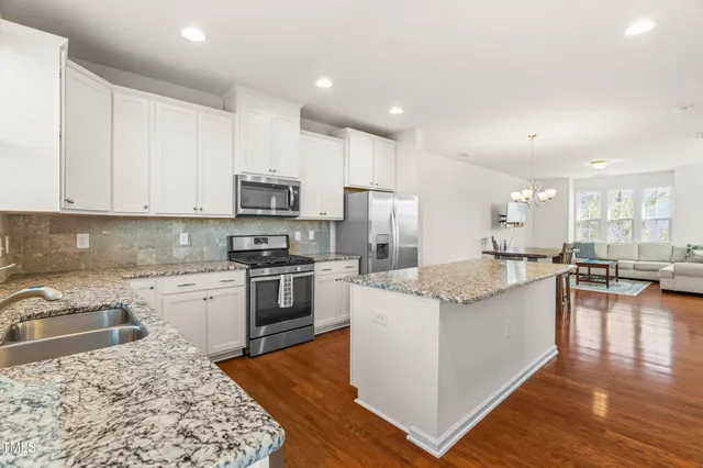 a kitchen with stainless steel appliances granite countertop a stove top oven a refrigerator a sink and a dining table with wooden floor