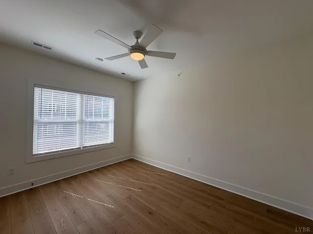 an empty room with wooden floor fan and windows