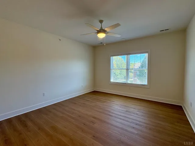 an empty room with wooden floor a ceiling fan and windows
