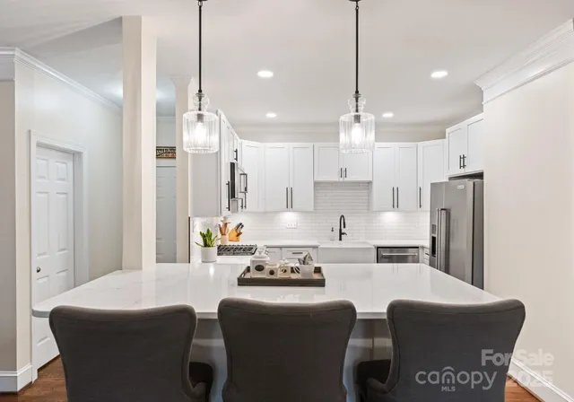 a kitchen with stainless steel appliances kitchen island granite countertop a dining table chairs and a refrigerator