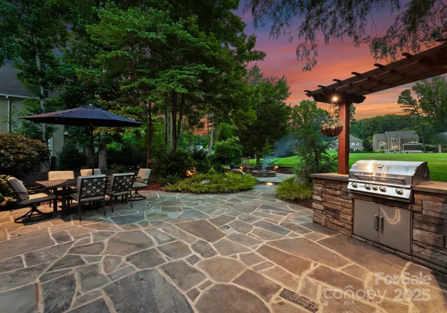 a view of a patio with table and chairs under an umbrella with a barbeque grill and wooden fence