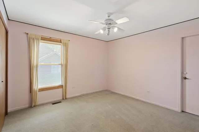 an empty room with a chandelier fan and wooden floor
