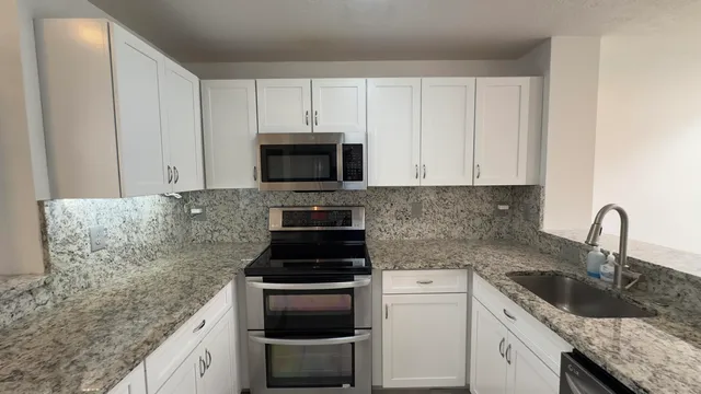 a kitchen with granite countertop white cabinets and stainless steel appliances