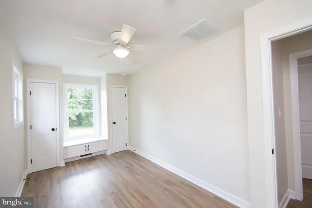 an empty room with wooden floor ceiling fan and windows