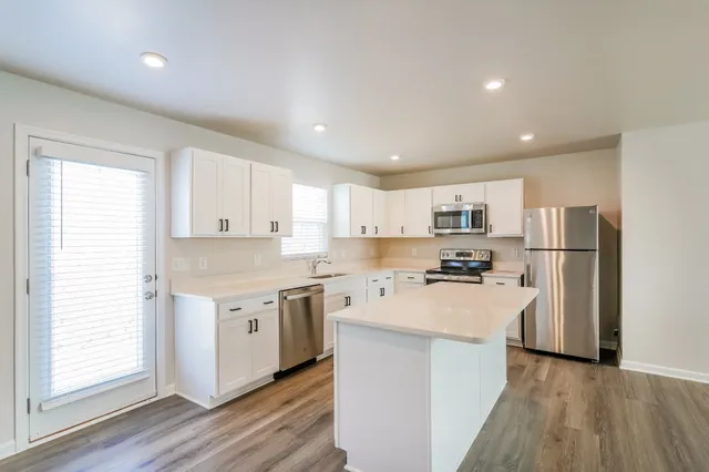 a kitchen with stainless steel appliances a refrigerator a stove a sink and white cabinets with wooden floor