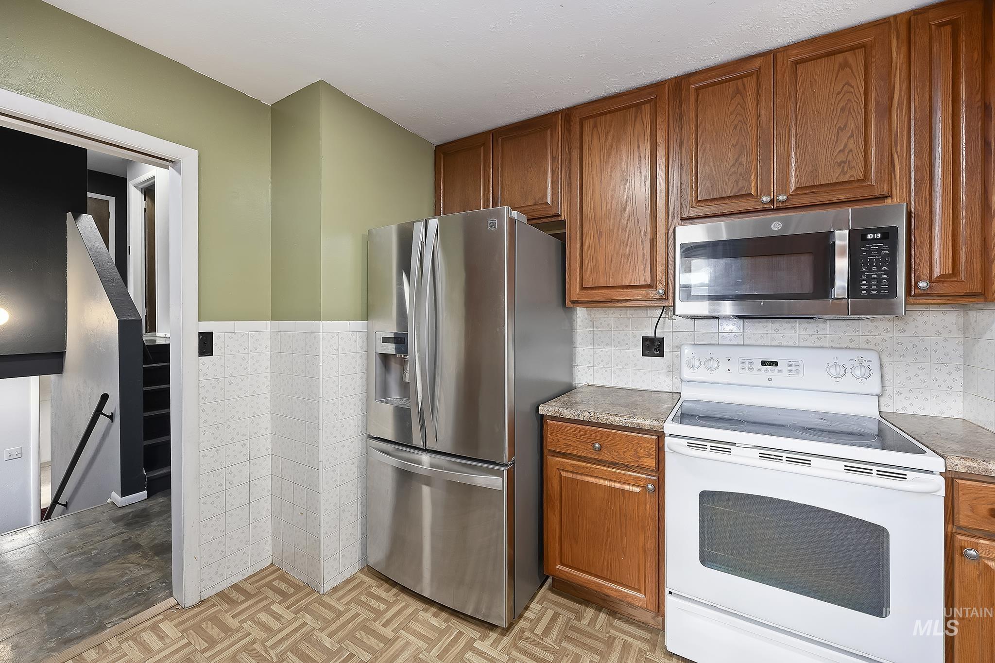 320 East 23rd Drive Burley, ID 83318 - Photo 15 of 34 Kitchen featuring stainless steel appliances, brown cabinetry, tile walls, and a wainscoted wall