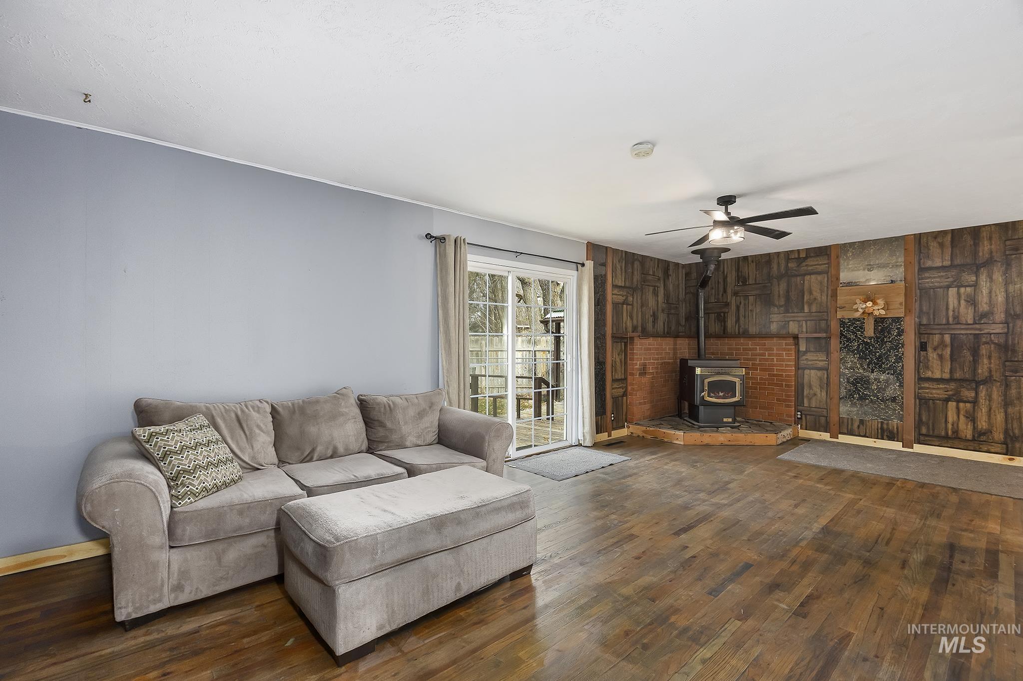 320 East 23rd Drive Burley, ID 83318 - Photo 5 of 34 Living area with a wood stove, dark wood finished floors, wood walls, and ceiling fan