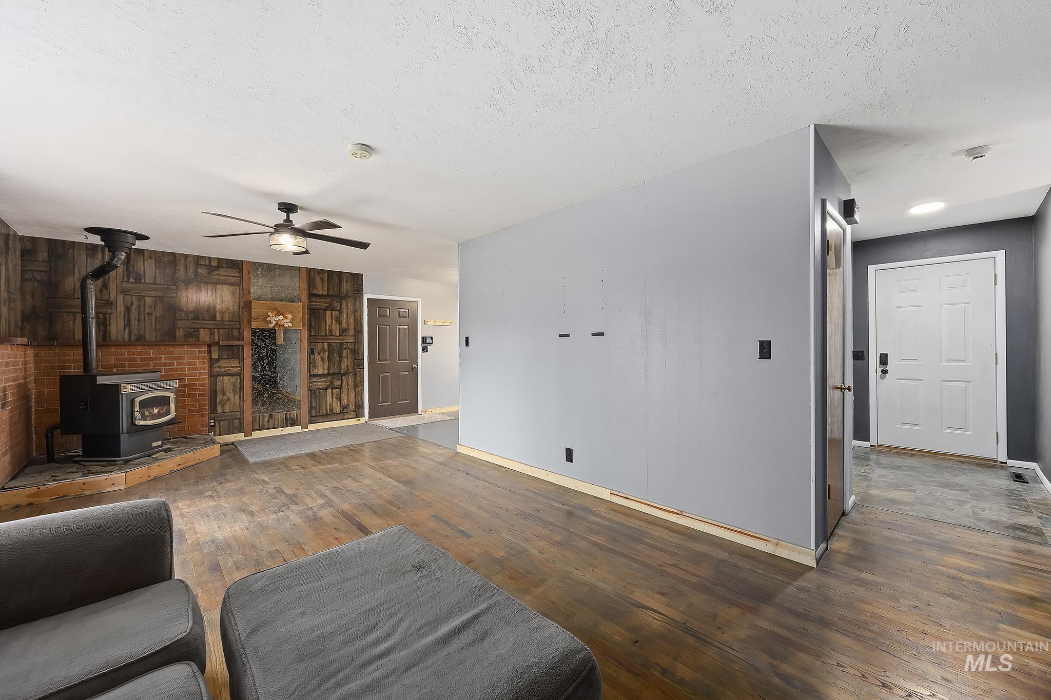 320 East 23rd Drive Burley, ID 83318 - Photo 8 of 34 Living room with a wood stove, wood-type flooring, wood walls, a textured ceiling, and a ceiling fan