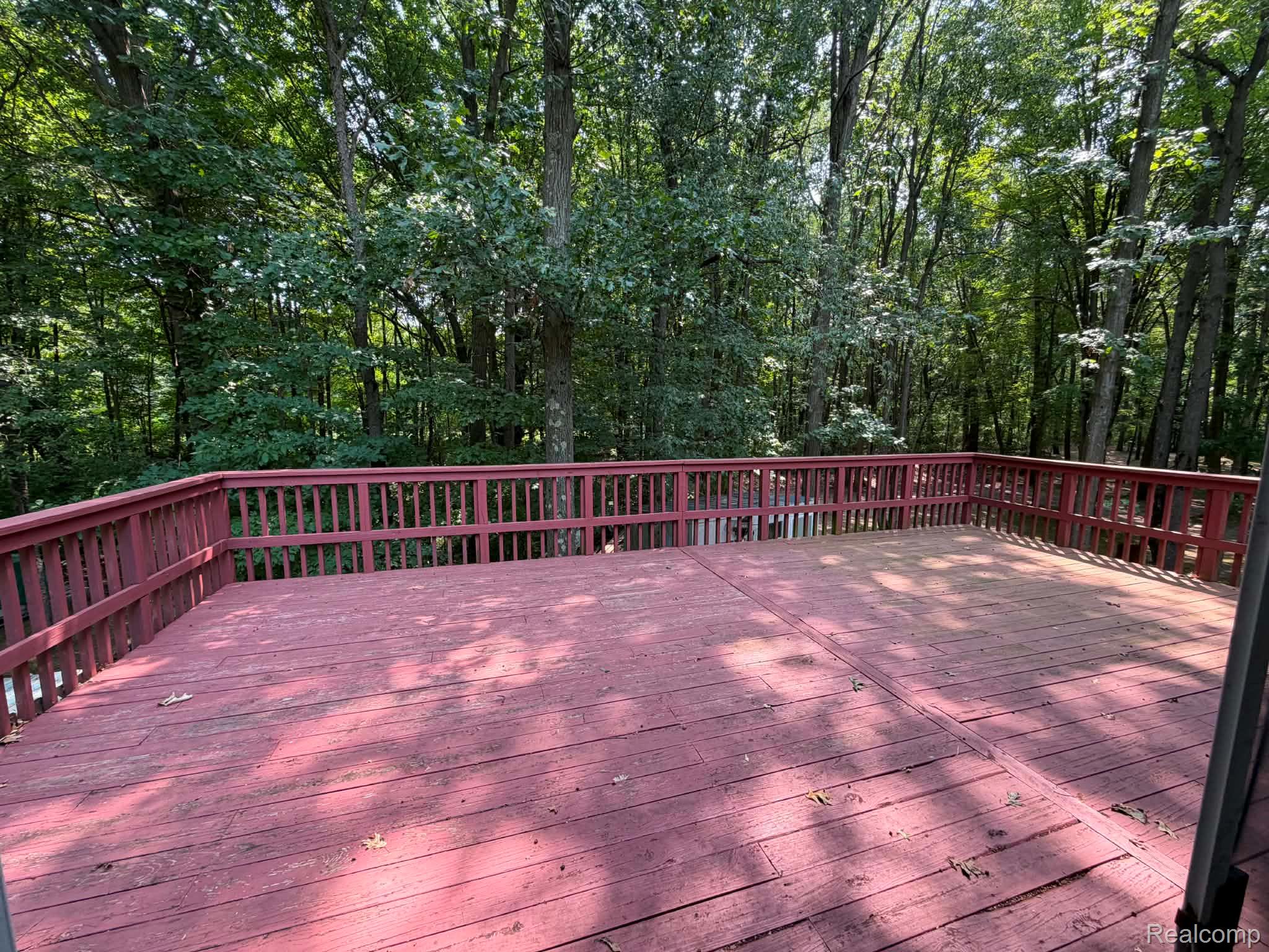 8110 North Latson Road Howell, MI 48855 - Photo 48 of 48 Expansive composite deck featuring a rich wood-finish surface and matching railings, surrounded by mature forest canopy providing natural privacy and shade