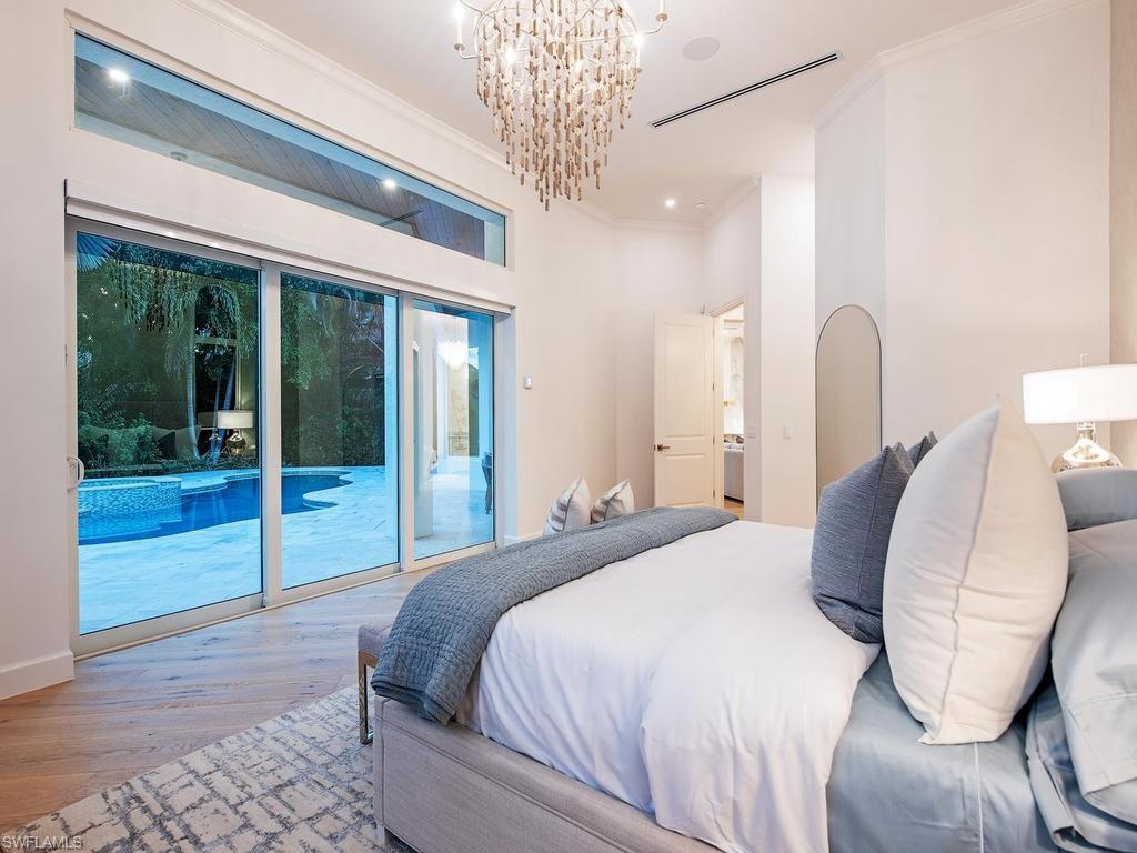 2363 Crayton Road Naples, FL 34103 - Photo 21 of 30 Bedroom featuring a large multi-panel sliding glass door, a transom window, wood-finish flooring, a contemporary chandelier, and recessed lighting