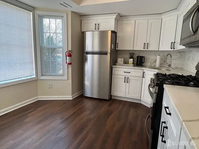 a kitchen with a refrigerator a stove a sink and white cabinets with wooden floor