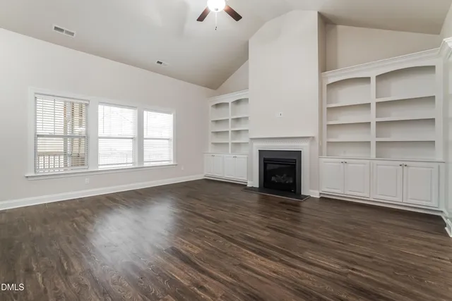 a view of an empty room with wooden floor fireplace and a window