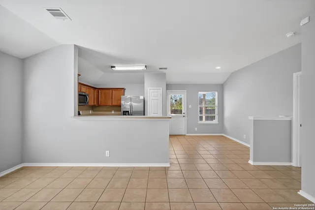 a view of an empty room with kitchen and window