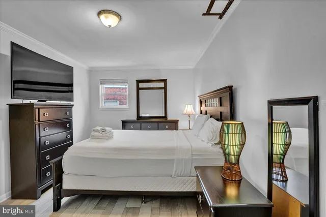 a bedroom with a bed a mirror on dresser and a flat screen tv