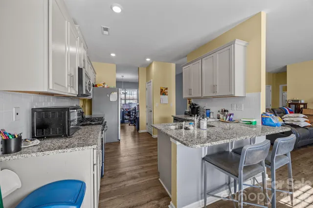 a kitchen with stainless steel appliances granite countertop a stove top oven a sink dishwasher a dining table and chairs with wooden floor