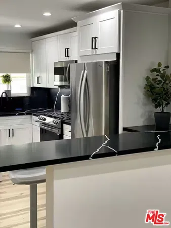 a kitchen with stainless steel appliances granite countertop a refrigerator a stove a sink and white cabinets