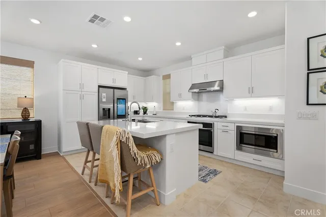 a kitchen with stainless steel appliances granite countertop a stove a sink a refrigerator and a dining table with white cabinets