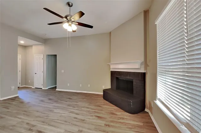 a view of an empty room with wooden floor a ceiling fan and a window