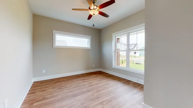 an empty room with chandelier fan and windows