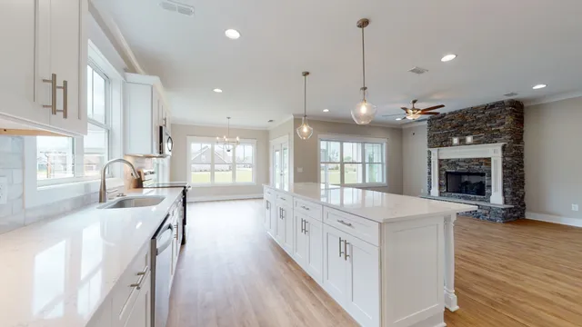 a large white kitchen with granite countertop a stove oven a sink dishwasher and a fireplace with wooden floor