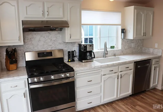 a kitchen with stainless steel appliances a refrigerator a stove a sink cabinets and wooden floor