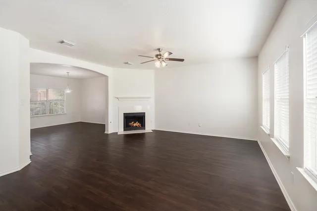 an empty room with wooden floor a chandelier fan and windows