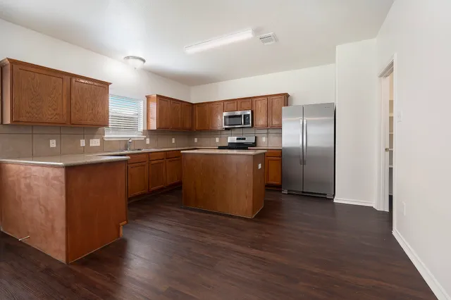 a kitchen with stainless steel appliances granite countertop a stove top oven a refrigerator and a sink with wooden floors