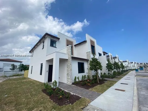 a view of a white house next to a yard with potted plants