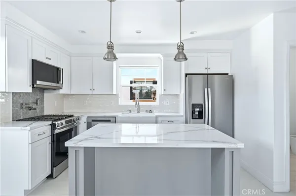 a kitchen with stainless steel appliances a sink a stove a refrigerator a center island and cabinets