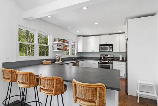 a kitchen with stainless steel appliances granite countertop a stove top oven a sink a dining table and chairs with wooden floor