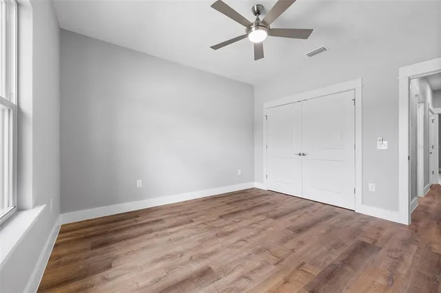 an empty room with wooden floor fan and windows