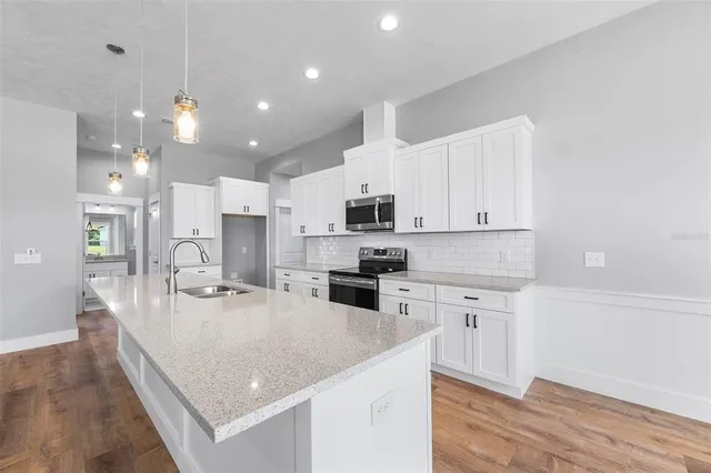 a large kitchen with kitchen island a stove a sink a refrigerator and white cabinets with wooden floor