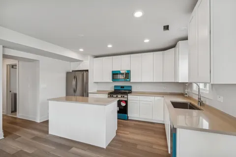 a kitchen with kitchen island a sink a stove a refrigerator and white cabinets with wooden floor