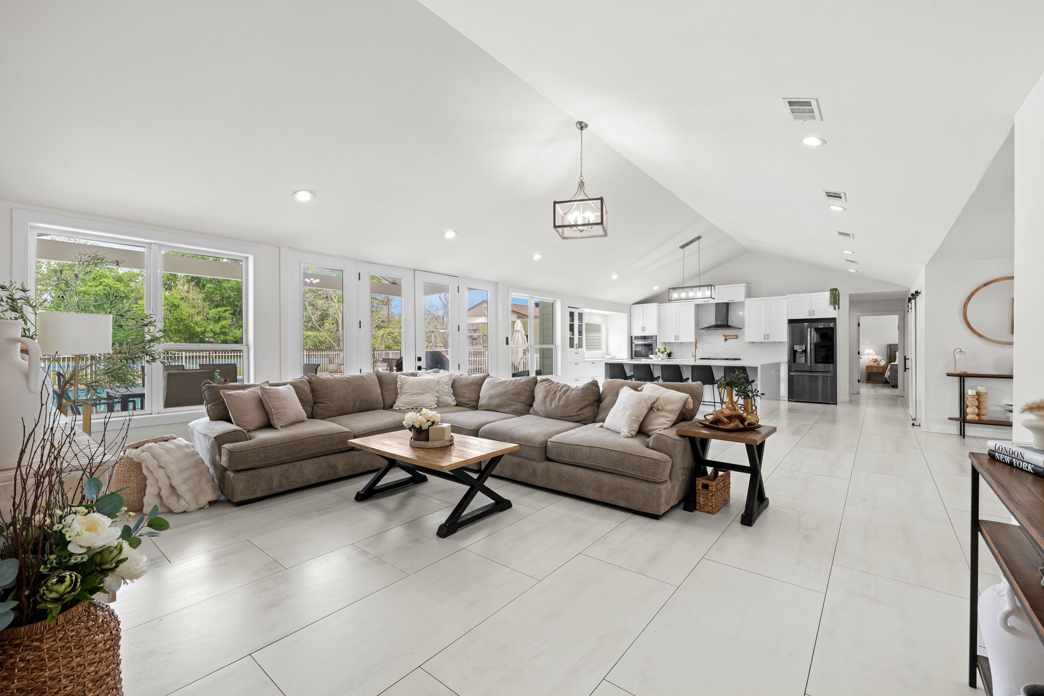 8800 Brae Acres Road Houston, TX 77074 - Photo 15 of 48 The French doors along the rear wall frame a direct view of the covered patio and pool. The kitchen reads clearly across the full open plan on the opposite end — the entire ground floor lives as one connected space.