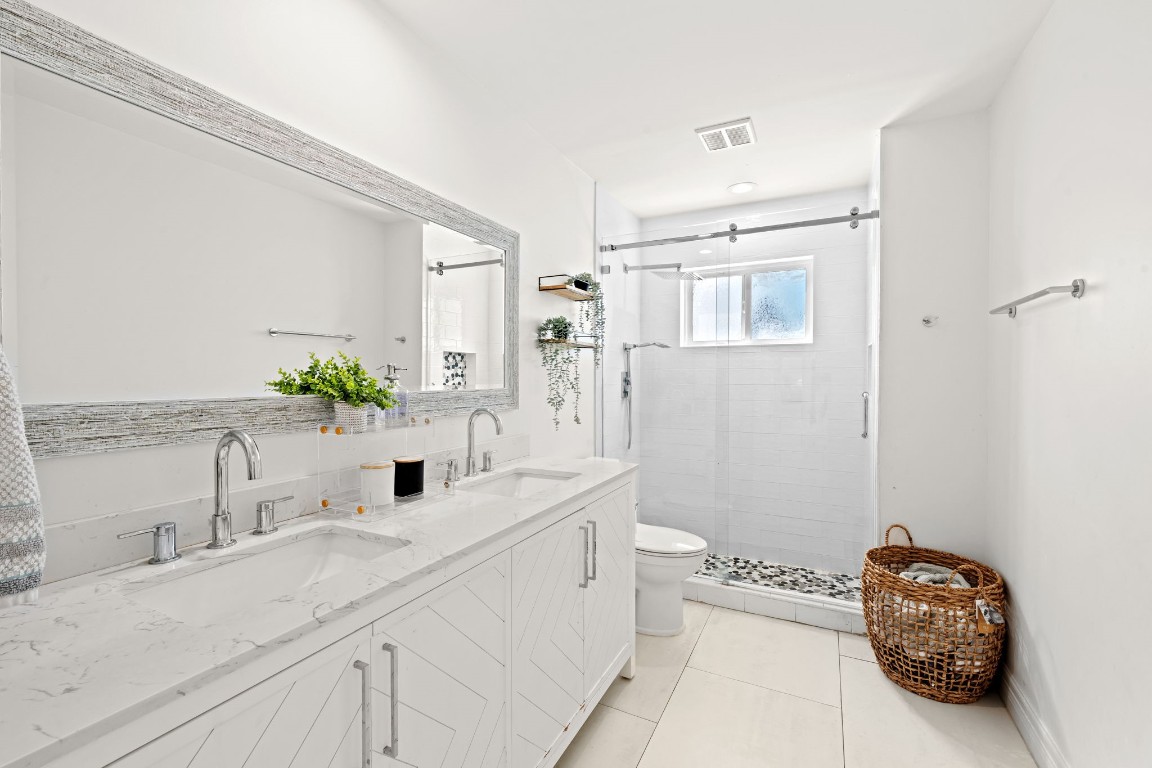 8800 Brae Acres Road Houston, TX 77074 - Photo 18 of 48 The shared secondary bathroom has a double vanity with herringbone-pattern cabinet fronts and brushed nickel hardware, topped with stunning bright countertop. A weathered wood-framed mirror spans the full width above both sinks, and a frameless sliding glass shower enclosure with white tile surround and penny tile floor ties together this functional secondary bathroom.
