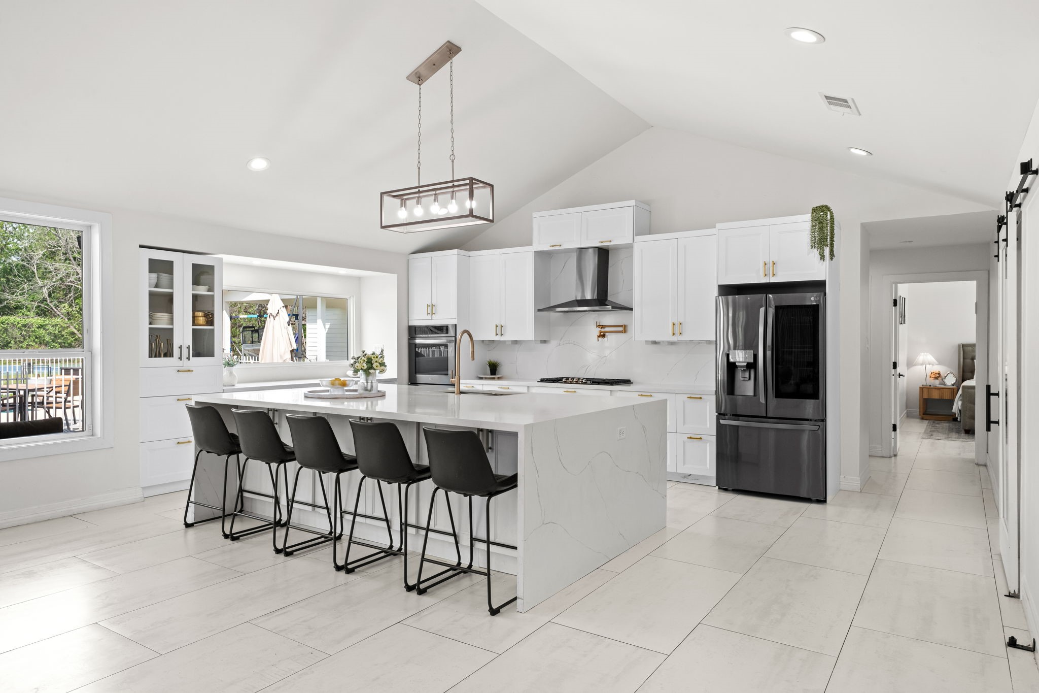 8800 Brae Acres Road Houston, TX 77074 - Photo 20 of 48 Seen from the dining area, the kitchen presents as a complete, well-organized room — island centered under the pendant, white shaker cabinetry running the full perimeter, vaulted ceilings above, and glass-front upper cabinets adding depth on the far wall.