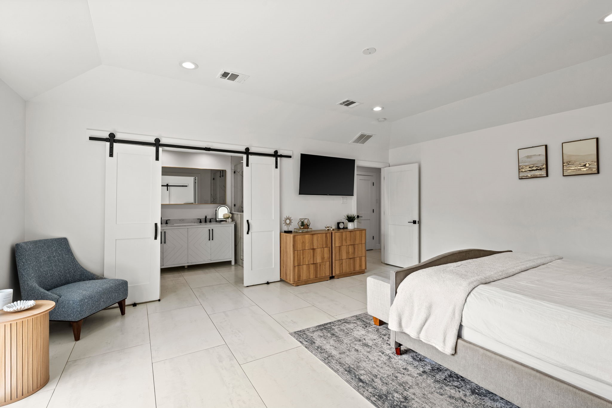 8800 Brae Acres Road Houston, TX 77074 - Photo 22 of 48 With the barn doors drawn open, the primary bath connection becomes immediate — gray cabinetry visible through the opening, the transition seamless between sleeping and bath.