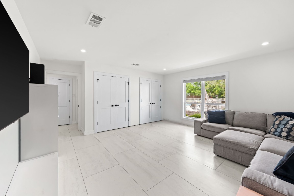 8800 Brae Acres Road Houston, TX 77074 - Photo 32 of 48 The game room has a footprint that changes based on how you use it — a full wall of double-panel closet doors provides more built-in storage than most dedicated utility rooms, while the window at the far end looks directly out to the yard and pool beyond. Whether it runs as a media room, playroom, or second living space, the large-format tile floors and recessed lighting keep the room from dictating the answer.