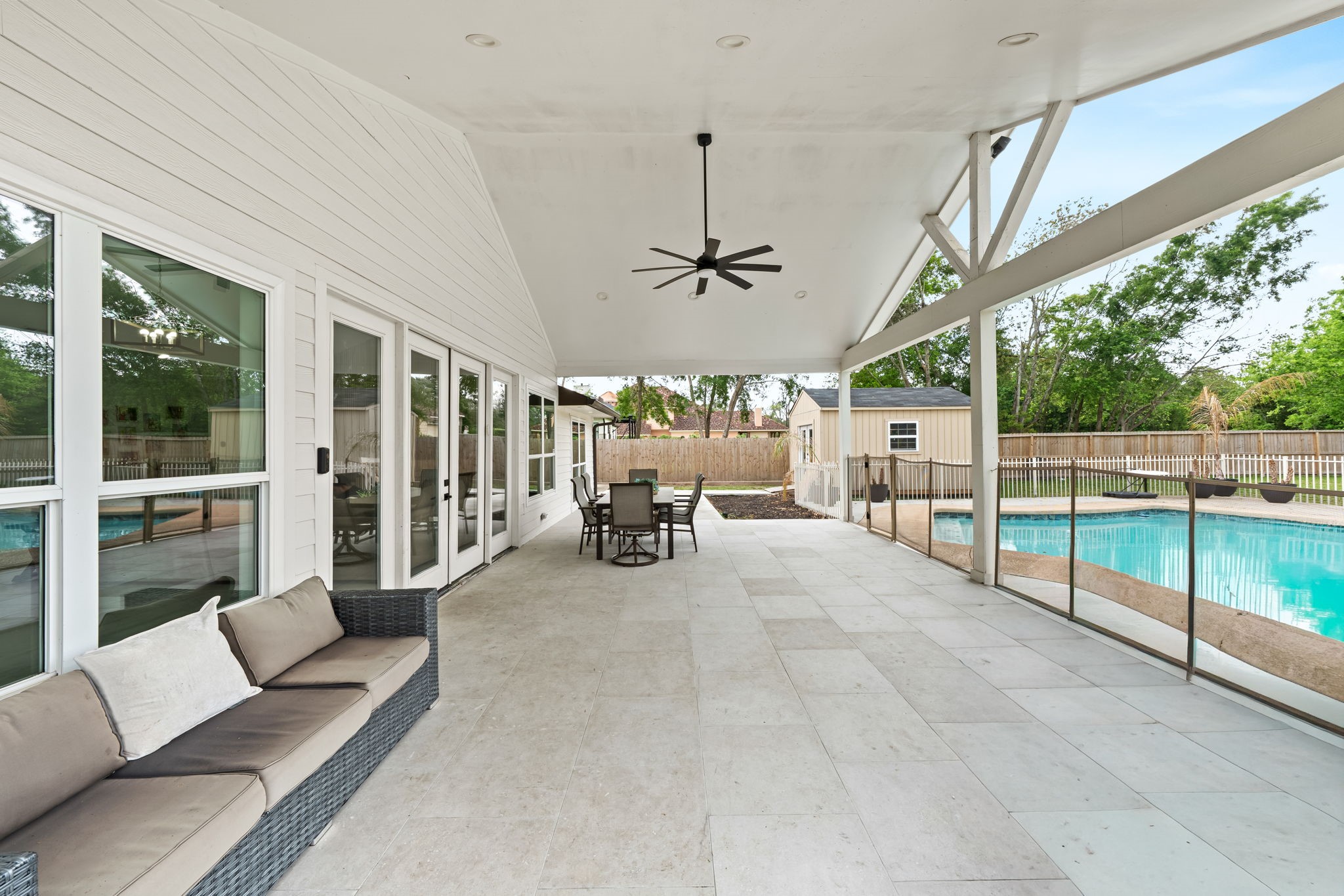8800 Brae Acres Road Houston, TX 77074 - Photo 33 of 48 This covered back patio is the kind of outdoor space that actually earns its square footage — a vaulted painted wood ceiling with exposed rafter detail, a matte black ceiling fan at the peak, and large-format travertine-look tile across the full deck. Multiple French doors connect back to the interior, creating seamless indoor / outdoor living.
