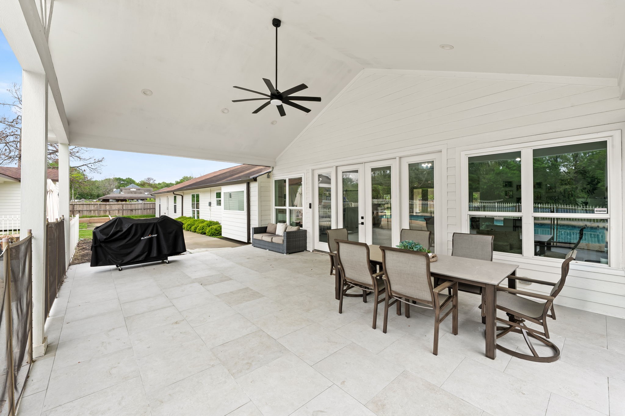 8800 Brae Acres Road Houston, TX 77074 - Photo 34 of 48 From this angle, the patio's depth and zoning read clearly — a dedicated grill area anchors the far end while the center of the covered footprint holds the main gathering space, all under continuous shade from the vaulted structure. The detached guesthouse is visible beyond the left edge, and the pool fence closes the right side, putting everything within a few steps of each other.