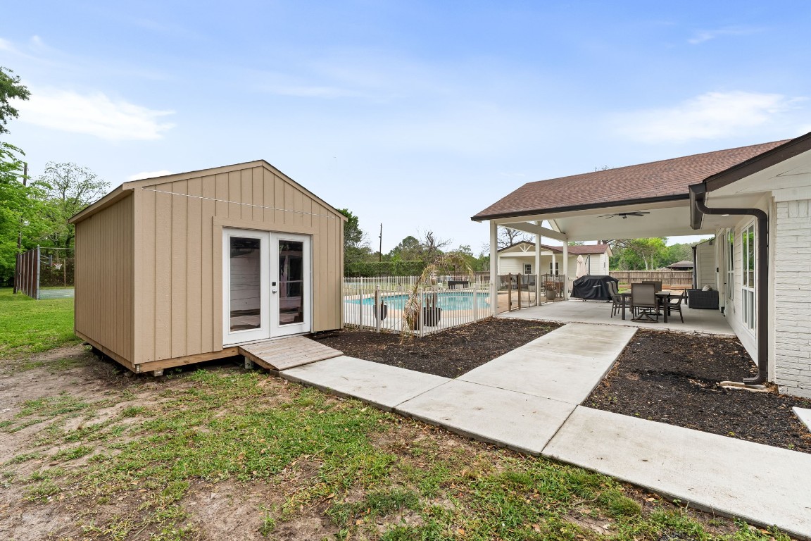 8800 Brae Acres Road Houston, TX 77074 - Photo 35 of 48 A detached storage building with vertical board-and-batten siding and double French doors sits on its own concrete pad at the mid-lot point — enough interior clearance for equipment, tools, or the kind of overflow storage a main house rarely has room for.