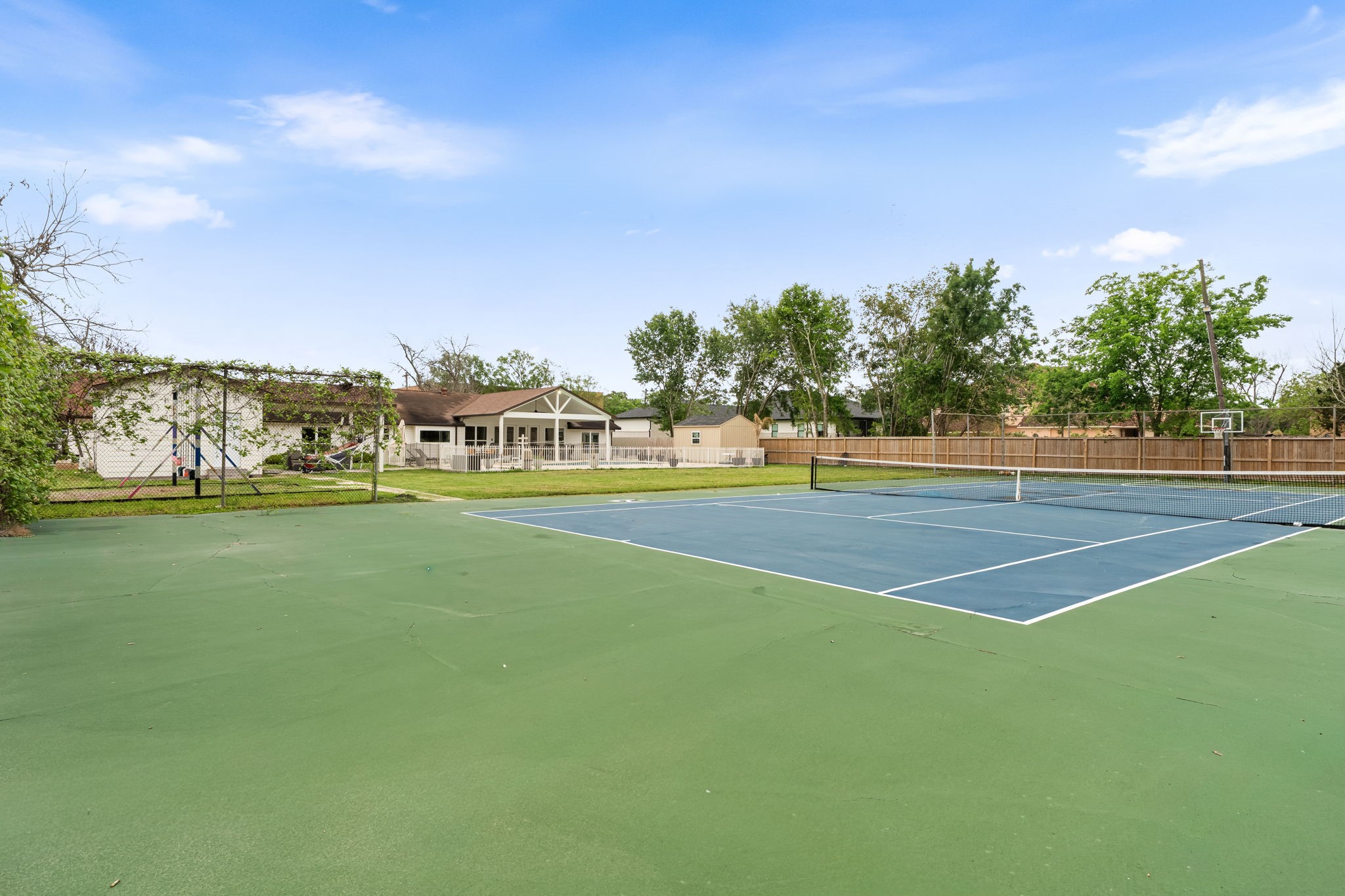 8800 Brae Acres Road Houston, TX 77074 - Photo 42 of 48 A full regulation tennis court with green and blue sport-court surfacing, a permanent net, and a basketball goal mounted at the far end — dual-sport without any additional footprint.