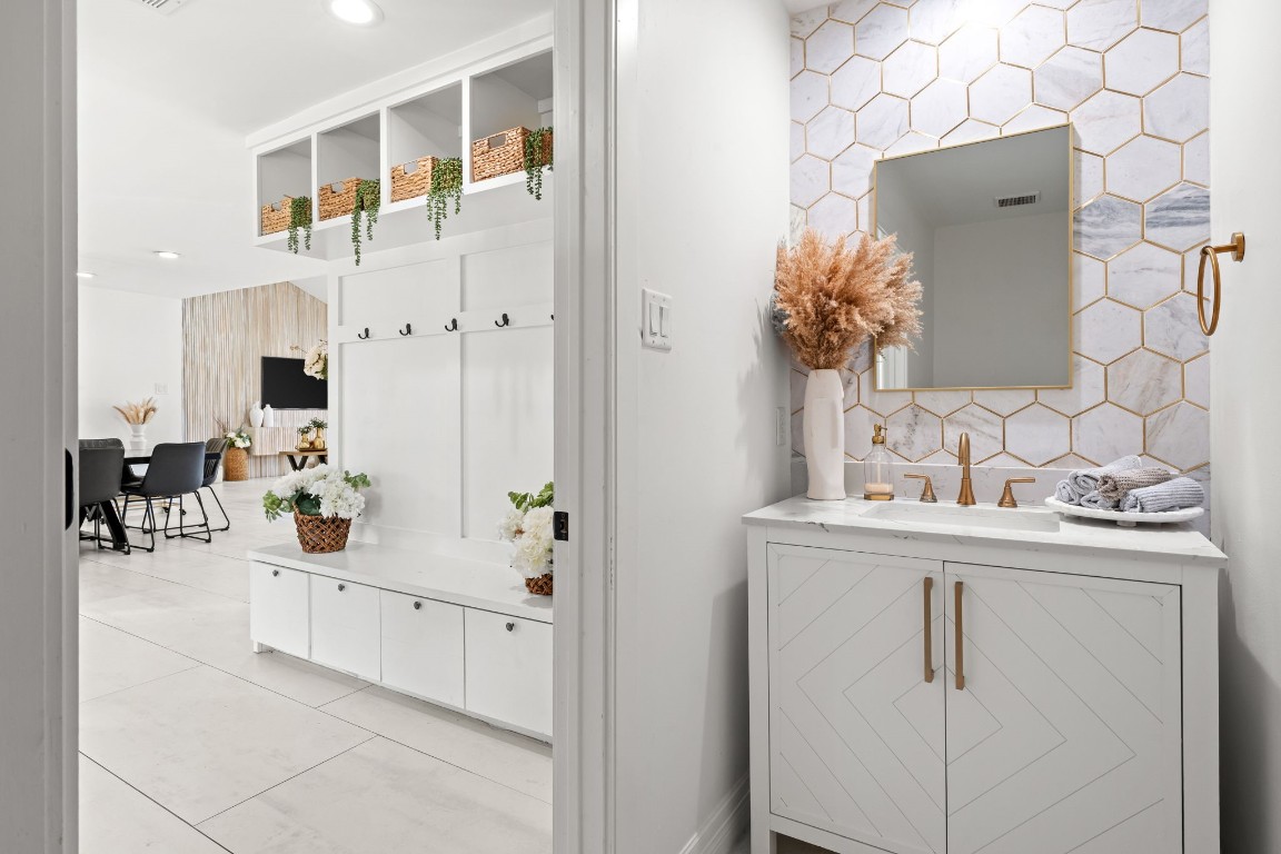 8800 Brae Acres Road Houston, TX 77074 - Photo 7 of 48 The powder room makes a statement in a small footprint — a herringbone-front white cabinet with brushed gold hardware, white quartz countertop with a gold gooseneck faucet, and a large-format hexagonal tile backsplash in white and gray with gold grout running to the mirror line. The gold-framed rectangular mirror ties the palette together.