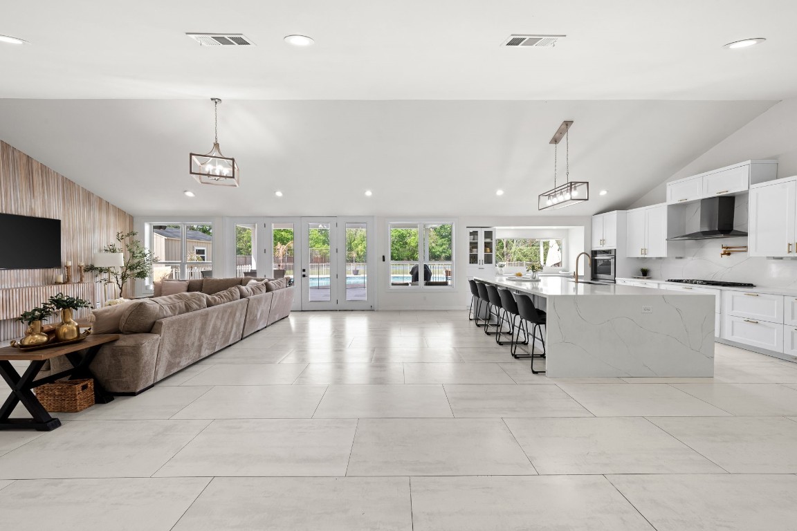 8800 Brae Acres Road Houston, TX 77074 - Photo 8 of 48 This is the view that puts the home in context — kitchen island on the right, wood-slat adorned family room on the left, French doors to the pool at the far end, and soaring ceilings with continuous large-format tile holding it all together.