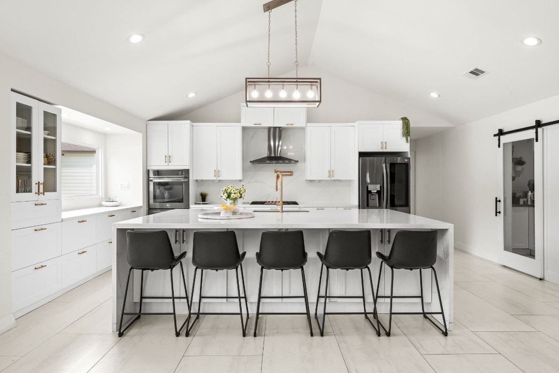 8800 Brae Acres Road Houston, TX 77074 - Photo 9 of 48 This gorgeous and open kitchen is the focal point of the home — an oversized waterfall style island with ample seating sits beneath a cage-style lantern pendant hanging from the vaulted ceiling, with white shaker cabinetry and brushed gold hardware wrapping the full perimeter.
