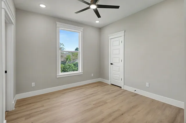 an empty room with wooden floor ceiling fan and windows