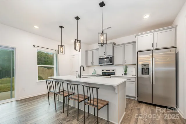 a kitchen with stainless steel appliances granite countertop a sink a refrigerator a kitchen island a table and chairs