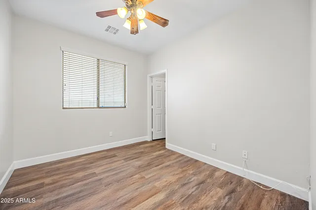 an empty room with wooden floor chandelier fan and windows