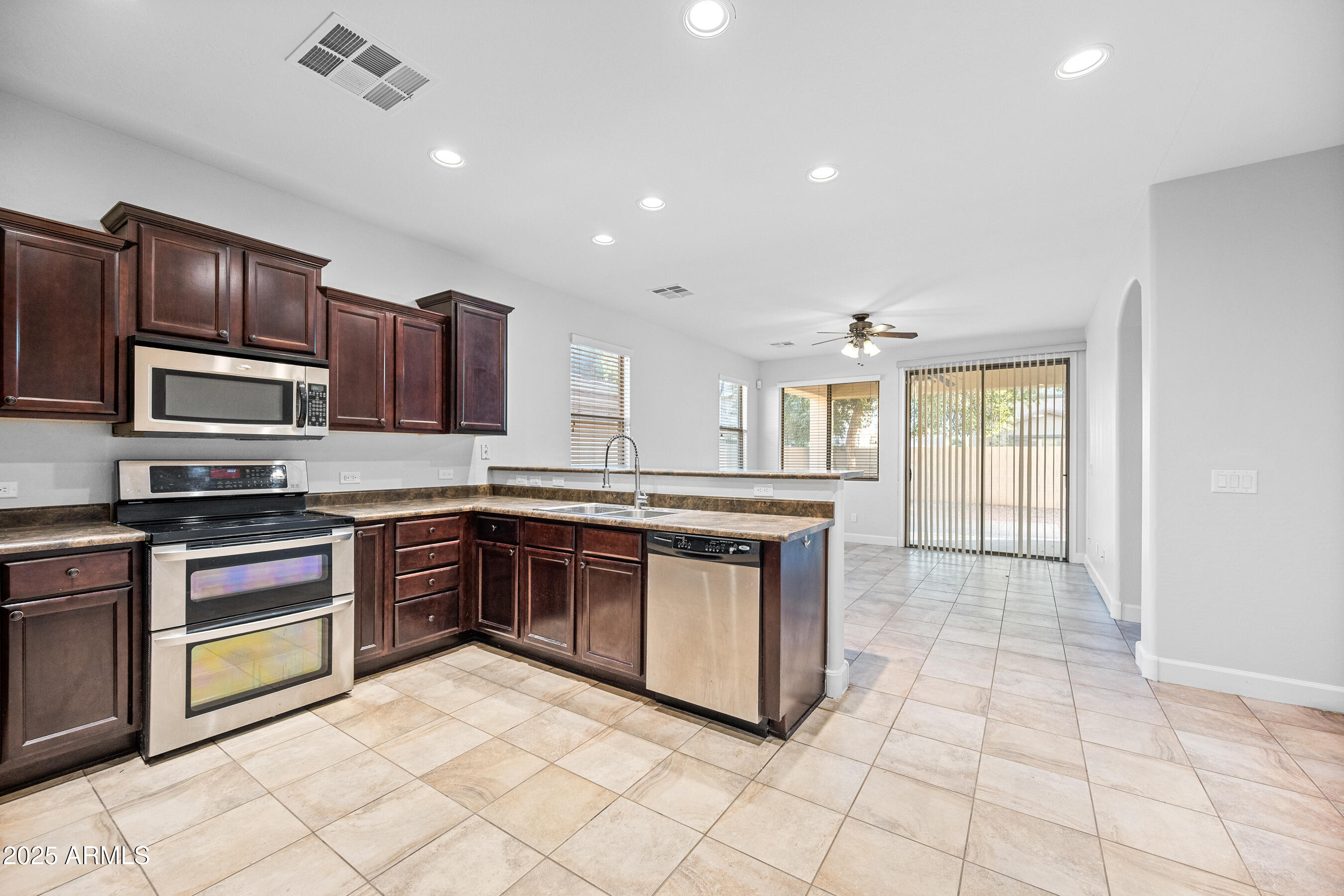 10805 West Woodland Avenue Avondale, AZ 85323 - Photo 6 of 25 a large kitchen with stainless steel appliances granite countertop a stove top oven a sink dishwasher a dining table and chairs with wooden floor